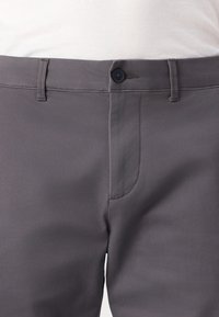 Graue Hose aus glattem Stoff, mit Knopfverschluss, Gürtelschlaufen und einer Seitentasche mit minimaler Naht.