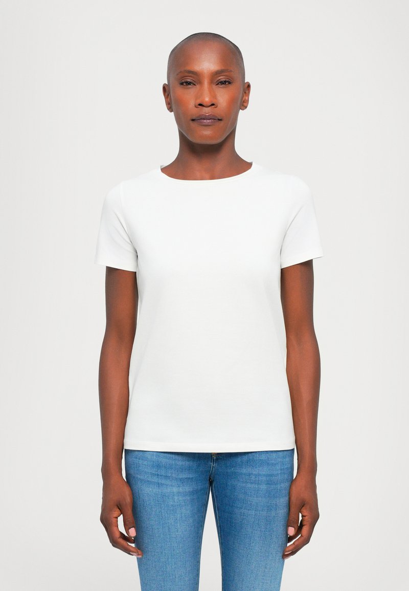 T-shirt bianco a maniche corte con scollatura rotonda, realizzato in tessuto morbido, abbinato a jeans blu slim fit, esposto su uno sfondo neutro.