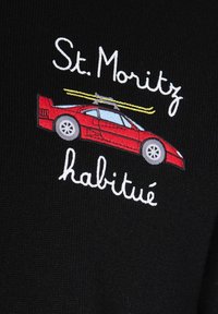 Auto sportiva rossa con sci gialli sul tetto, ricamata sopra e sotto con la scritta "St. Moritz habitude" su sfondo di tessuto nero.