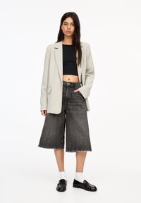 Hellgrauer Blazer, schwarzes Crop-Top, hochtaillierte graue Denim-Culottes. Schwarze Loafers und weiße Socken runden das Outfit ab.