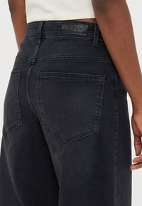 Čierne džínsy z denimu s stredne vysokým pásom, zadnými vreckami s zakrivenými švami a koženou značkovou nášivkou na páse. Hladká textura.
