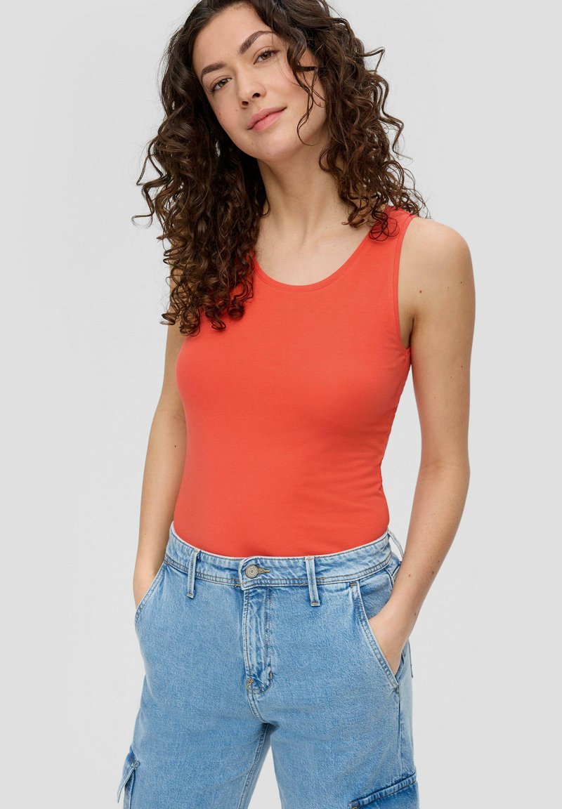 Rotes ärmelloses Top aus weichem Stoff, kombiniert mit hellblauen Denim-Cargo-Hosen, die große Seitentaschen und eine lockere Passform haben.