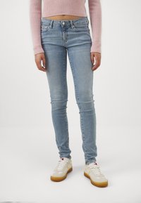 Jeans ajustados de denim azul claro con cintura media, un ligero desgaste y cinco bolsillos, combinados con zapatillas blancas.