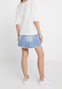 Jeanskjol med en något fransad kant och sidoklyfta, kombinerad med en lös vit topp och vita sneakers med beige detaljer.