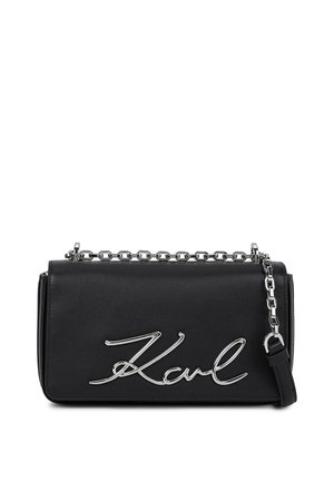Bolso de cuero negro con una correa de cadena plateada, que presenta un destacado logo metálico "Karl" en cursiva en la parte frontal. Forma rectangular.