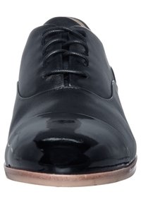 Chaussure habillée en cuir noir avec une finition lisse, un bout arrondi et une semelle plate. Les lacets sont centrés, avec un détail poli au bout.