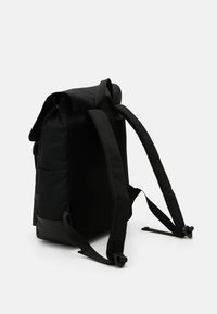 Sac à dos noir avec un design à ouverture roulante, doté de côtés en mesh, de bretelles réglables et de contrastes de texture distincts. Matériau durable avec une quincaillerie minimale.