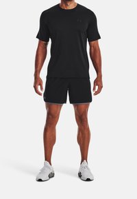 Svart atletisk t-shirt och shorts i fuktavledande tyg. Har en subtil logotype och kontrasterande ljus trim på shortsen. Vita sneakers.