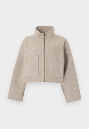 Cropped beige jacket made of soft fabric, featuring a high collar, front zipper, and two large flap pockets on the chest.