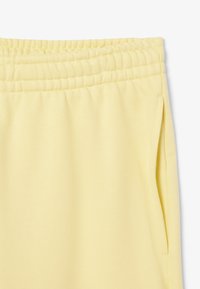 Pantalones de chándal amarillos con cintura elástica, con bolsillos laterales, textura suave y un corte relajado. Diseño simple, tejido ligero adecuado para uso casual.