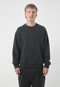 Schwarzer Sweatshirt aus Baumwolle. Mit Rundhalsausschnitt, langen Ärmeln und gerippten Bündchen. Kombiniert mit schwarzen Hosen. Minimalistisches Design.