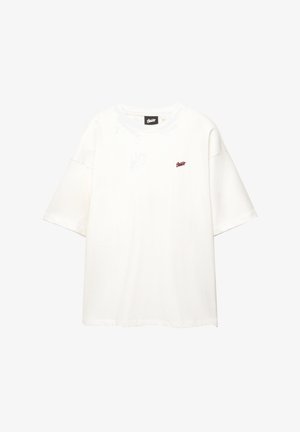 T-shirt oversize blanche en coton, avec des manches courtes et un petit logo rouge sur la poitrine. Encolure ronde, design minimal.