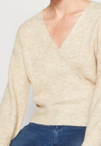 Beżowy sweter dzianinowy z gł�ębokim dekoltem w kształcie litery V, długimi rękawami i prążkowaną fakturą. Miękka tkanina z subtelnymi odcieniami kolorów.