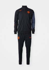 Fekete Nike tréningruházat narancssárga részletekkel, zipzáras dzsekivel, hosszú ujjal és hozzáillő nadrággal, sima, rugalmas anyagból.