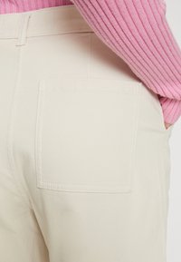 Ljust beiga byxor har en framträdande bakficka med en rak, ren design och subtil sömnad. Tyget ser slätt och hållbart ut.