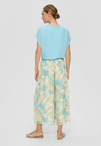 Haut bleu clair à manches courtes associé à un pantalon large à motifs avec des designs paisley dans des couleurs pastel. Des sandales complètent la tenue.