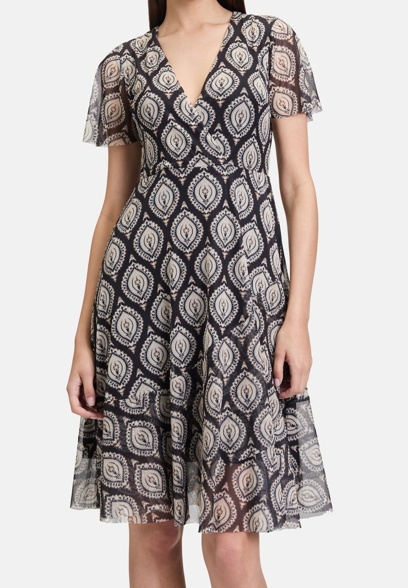 Femme portant une robe à motifs noir et blanc avec des manches courtes transparentes et un décolleté en V.