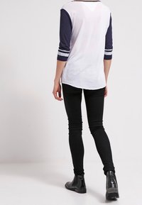 Valkoinen ja laivastonsininen pitkähihaisen paita kontrastivärisillä hihoilla, yhdistetty mustiin skinny-farkkuihin ja mustiin nilkkureihin. Sileä kangas, rento istuvuus.