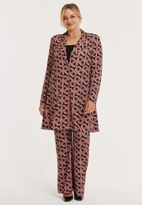 Geprinte pakken set met een lange blazer en bijpassende broek, gemaakt van stof met grote roze en zwarte ovale patronen op een donkere achtergrond.
