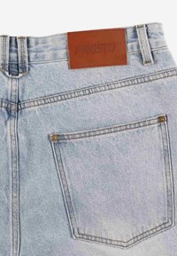 Jasnoniebieskie dżinsy z denimu z brązową skórzaną naszywką z napisem "PROSTO" z tyłu. Posiadają klasyczny krój z pięcioma kieszeniami i kontrastowe szwy.