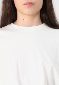 Balta medvilninė marškinė su apykakle, trumpomis rankovėmis ir glotnia, lengva tekstūra, pavaizduota prieš neutralaus fono.