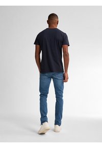 Camiseta de manga corta en color navy, jeans de mezclilla azules y zapatillas blancas. Diseño sencillo, forma ajustada, sin patrones ni gráficos visibles.