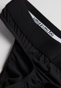 Sous-vêtements noirs avec une texture lisse, une taille élastique arbore un logo blanc et de légers fronces sur les côtés pour un look ajusté.