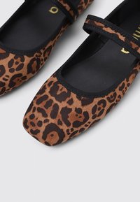 Chaussures plates en imprimé léopard, avec une partie supérieure en textile doux marron et noir, un bout rond, et une sangle élastique noire sur le cou-de-pied.