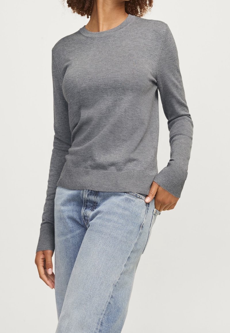 Grå långärmad stickad tröja med rund halsringning och ribbade ärmslut, parat med ljusblå jeans. Mjuk textur och figursydd design.