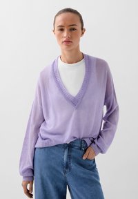 Lavendel V-hals trui van zachte stof met een geribde zoom, gedragen over een witte aansluitende top, gecombineerd met hoog getailleerde blauwe jeans.