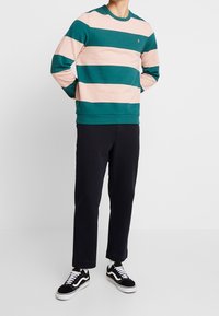 Pasiasty sweatshirt w kolorze turkusowym i różowym, materiał bawełniany, okrągły dekolt, ściągacze na rękawach, zestawiony z czarnymi spodniami i czarno-białymi sneakerami.