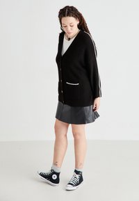 Czarny dzianinowy kardigan z dwoma przednimi kieszeniami, z dekoltem w serek i guzikami. Połączony z czarną skórzaną spódnicą i czarnymi trampkami za kostkę.