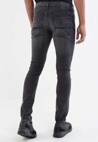 Pantalones vaqueros ajustados de mezclilla negra con una textura desgastada, que presentan una cintura de altura media, cinco bolsillos y detalles de costura sutiles en la parte posterior.