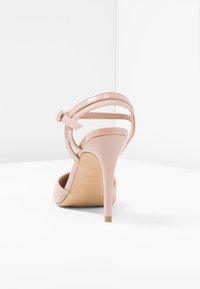 Vaaleanpunaiset korkeakorkoiset sandaalit, joissa on kiiltävä pinta, ohuet stiletto-korkokengät ja useita säädettävissä olevia remmejä nilkassa.