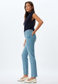 Jeans de denim azul con corte recto, complementados con una blusa sin mangas en color azul marino y zapatos de tacón cuadrado blancos. Textura suave, diseño casual.