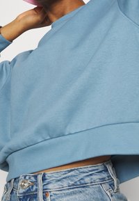 Sweat-shirt court bleu clair à manches longues, texture douce, et ourlet côtelé, associé à un jean en denim délavé taille haute.