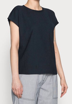 Top azzurro scuro a maniche corte con scollatura rotonda e un sottile motivo testurizzato. Abbinato a pantaloni a gamba larga a righe grigie chiare.