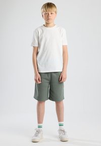 T-shirt bianca a maniche corte, pantaloni corti verdi, sneakers bianche con dettagli grigi e calze a righe. Design semplice con una vestibilità rilassata.