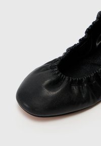 Balerini din piele neagră, cu vârful rotunjit și margine elasticizată. Au o textură netedă și un luciu subtil pe suprafață.