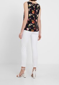 Top sin mangas con estampado floral en azul marino y cuello redondo, combinado con jeans blancos ajustados y sandalias blancas de tacón bloque.
