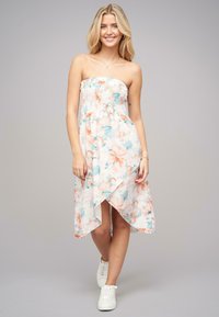 Blomstrete, stroppeløs midikjole med smocket topp, med myke pastellfarger, en asymmetrisk hem og lett stoff. Brukt med hvite sneakers.