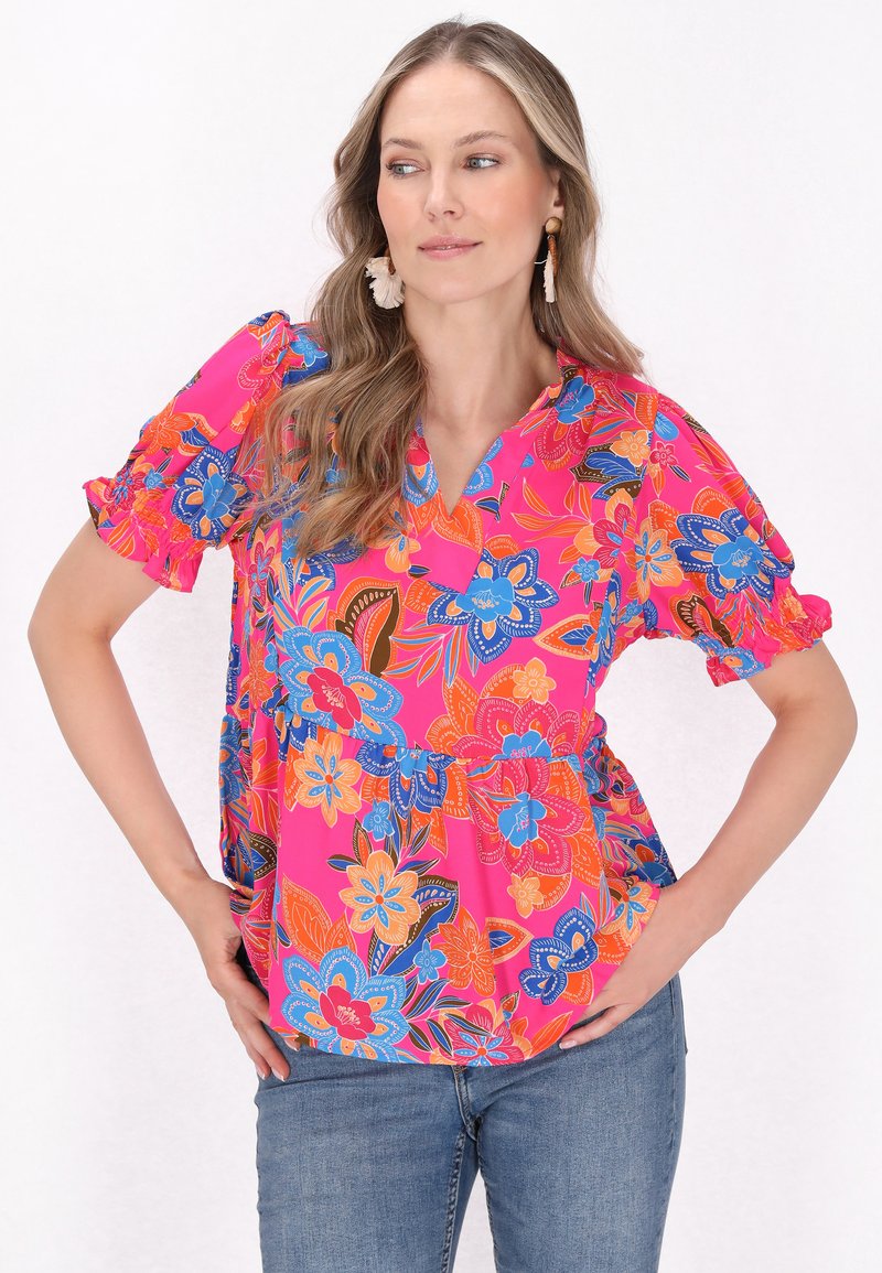 Blomstret bluse i lys pink med blå, orange og sorte accenter. Har korte, rynkede ærmer, en V-hals og en afslappet pasform.