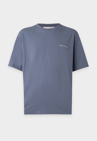 Απλό μπλε T-shirt με κοντά μανίκια και μικρό λευκό κείμενο "Tiger of Sweden" στο αριστερό στήθος σε λευκό φόντο.