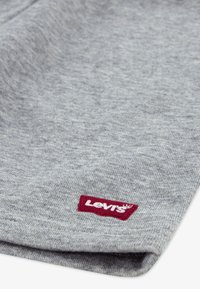 Tissu gris, texture douce ; présente une étiquette logo Levi's rouge cousue près de l'ourlet. Design simple avec un bord plié.