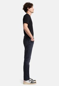 Schlanke, dunkelblaue Jeans mit mittelhohem Bund, ausgestattet mit einem Fünf-Taschen-Design und subtilen Nähdetails; kombiniert mit einem schwarzen T-Shirt und Sneakers.