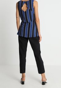 Marinblå ärmlös topp med vertikala vita ränder, utställd nederkant och nyckelhålssnitt på baksidan. Kombineras med svarta avsmalnande byxor och klacksandaler.