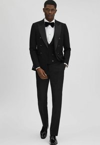 Tuxedo nero con giacca doppiopetto, revers a punta e dettagli dorati. Include una camicia bianca e un papillon nero. Pantaloni slim-fit e scarpe lucide.