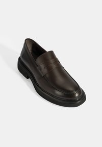 Bruine leren loafers met een gladde afwerking, voorzien van een decoratieve band en een platte rubberen zool, ontworpen voor casual of formele gelegenheden.