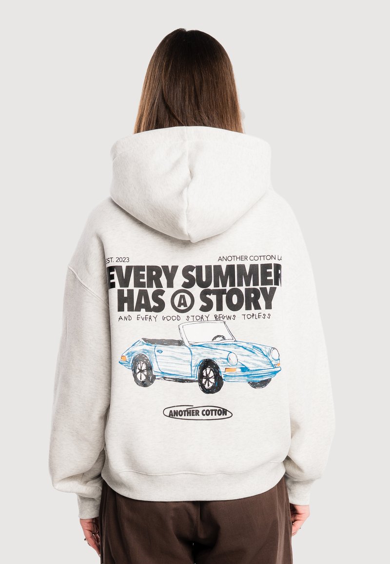 Personne portant un sweat à capuche blanc avec le texte « Every summer has a story » et un dessin d'une voiture décapotable bleue dans le dos, tournée de dos.