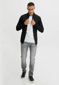 Sort strikket cardigan med høj krave, båret over en hvid T-shirt. Sammen med lysegrå jeans og sorte sneakers.